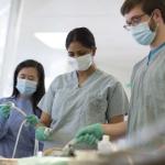 3 medical students wearing scrubs, masks, and gloves, working together