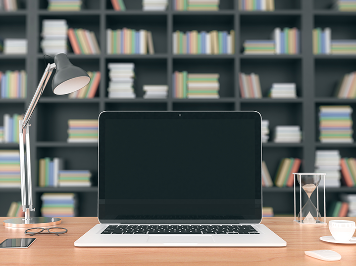 Photo of an open laptop, on a desk, in front of a large bookshelf