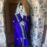 Dr. Lady J stands in full drag makeup and a long, ornate blue robe with a large butterfly clip in her hair.