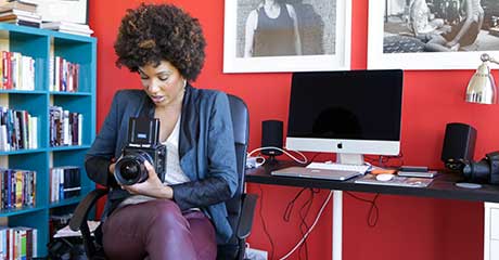 Photo of LaToya Ruby Frazier sitting at a desk and holding a camera