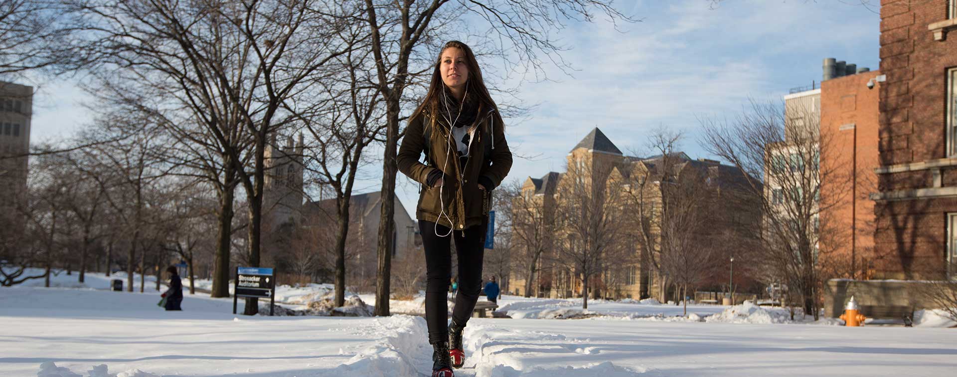 Photo of female student walking across campus surrounded by snow