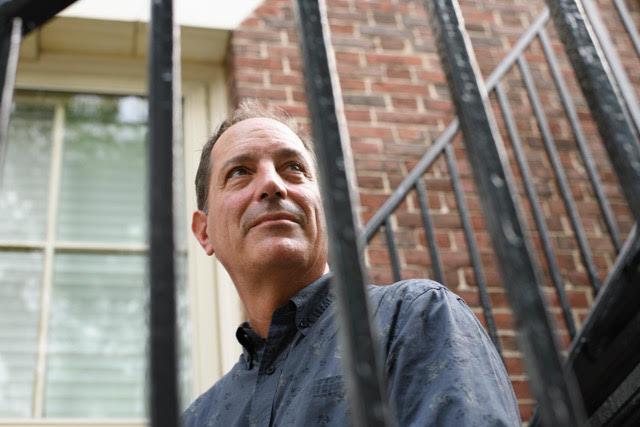 Rob Verchick sitting in front of a brick wall, partially obscured by stair railings