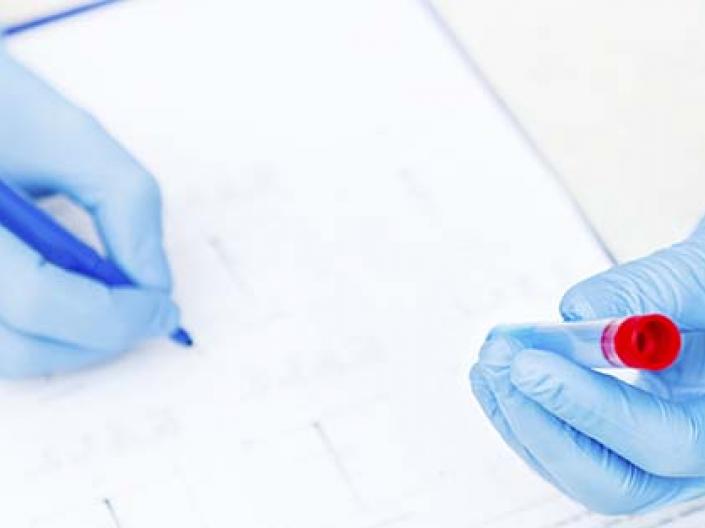 Image of scientist with blue latex gloves holding a test tube with a red top while writhing results onto a form 