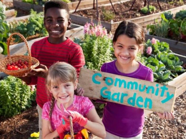 Children in a garden holding a garden holding a Community Garden sign
