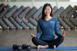 Woman in yoga pose sitting on floor with dumbbells