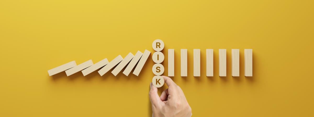 Top view wooden of a hand placing wooden block letters reading "risk" against a yellow backdrop