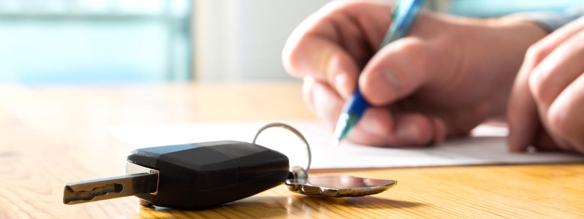 Close up image of hands signing paper on table next to a car key
