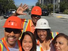 Group of 5 people wearing construction outfits smiling at the camera