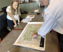 Man pointing at large map on table while young woman looks on.