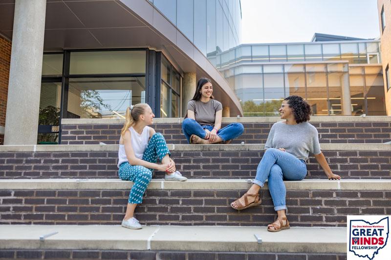 Three students sit on steps behind Mandel School patio