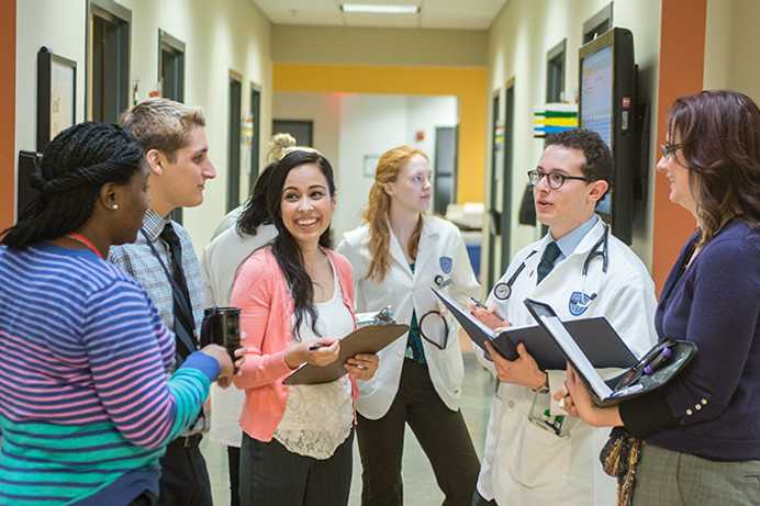 Photo of a group of Case Western Reserve University students, some in plain clothes and others in white coats, talking in a hospital setting