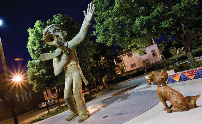 Statue of a boy playing trumpet with a dog statue watching