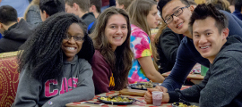 Four students at a table where they are eating and smiling for the camera