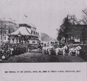 Black and white photo of a large procession that is passing an ornate coffin and memorial