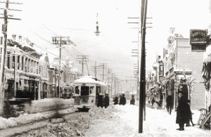 Black and white photo of a few people boarding a trolley on and otherwise deserted, snow covered street.
