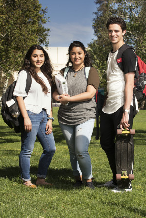 Three smiling students standing together on a college greenspace