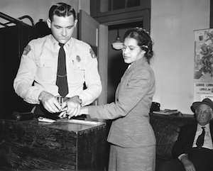 A black and white photo of Rosa Parks being fingerprinted by a police officer