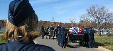 The back of the head of a woman in uniform, watching a military funeral