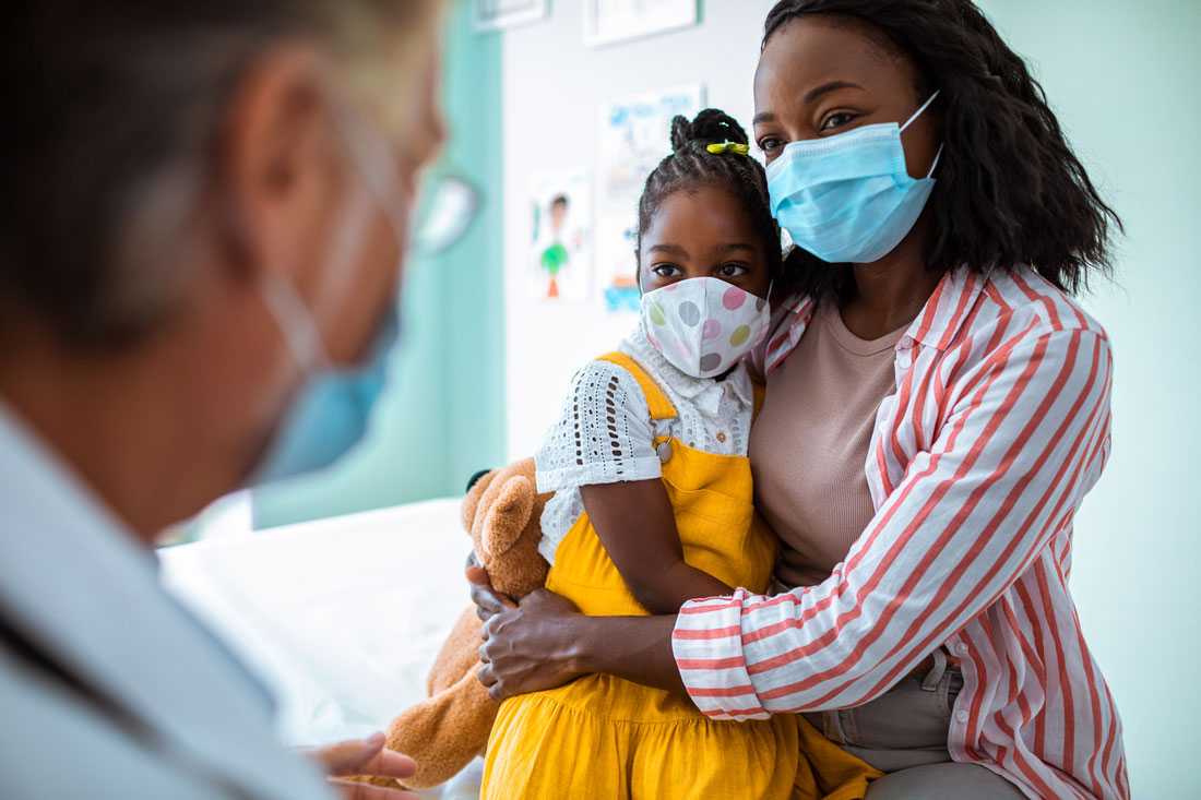 Photo of a mother and her daughter wearing masks while visiting with a pediatrician
