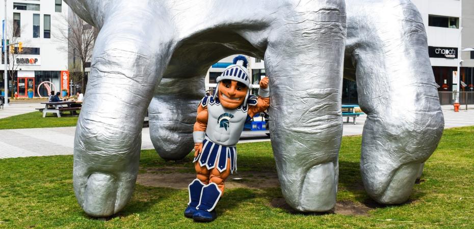 CWRU mascot standing beneath a sculpture of a hand.