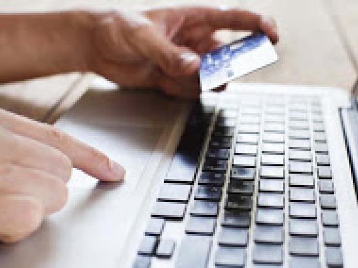 Person typing on a computer keyboard holding a credit card