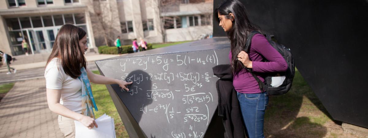 Two female students working on a math problem on a chalkboard in the center of the CWRU Quad.
