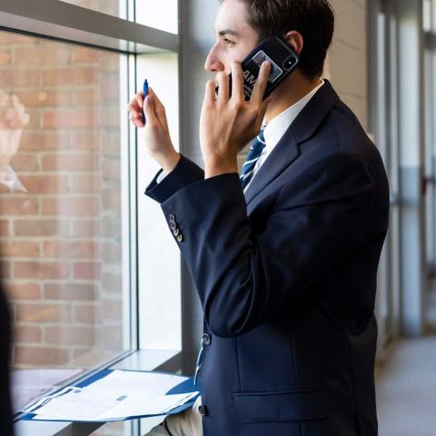 A student in a professional suit talks on a cell phone and looks out the window
