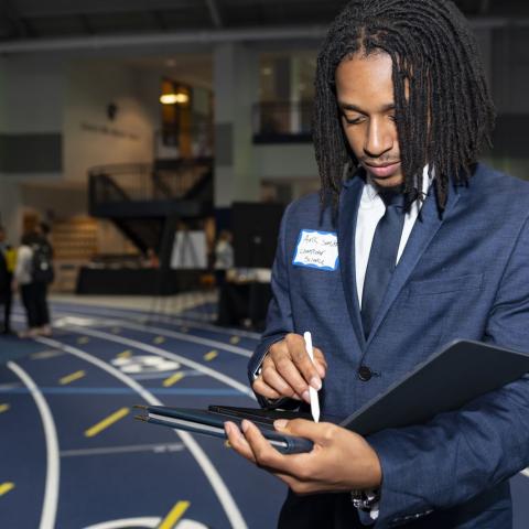 A student in a suit stands at the career fair and writes notes in a folio