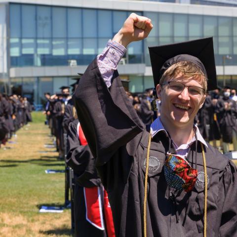 Student in cap and gown raising fist in celebration at outdoor graduation