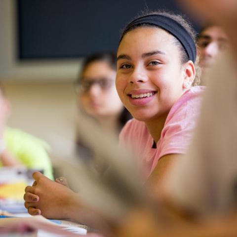 Students sitting in a class setting. One student smiling at the camera. 