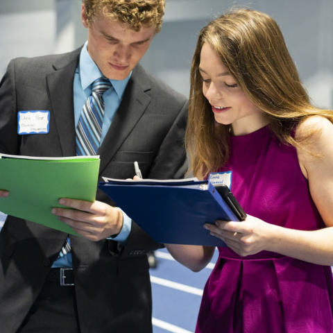 Male and female in business attire conferring on a paper held behind their binders