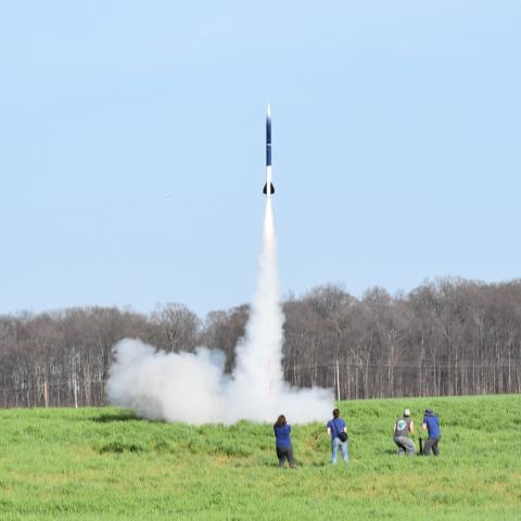 4 students watching a rocket launch in a field