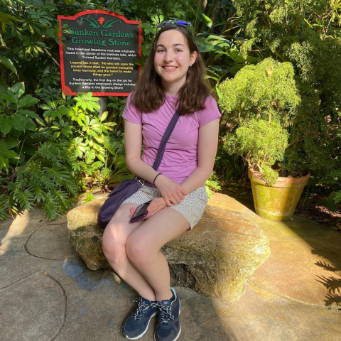 Girl sitting in front of bush and sign