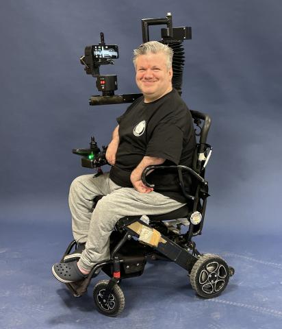 Man sitting in a wheelchair with a motorized arm for a swiveling gimbal, smiling at camera