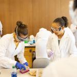 Students in a biology lab with goggles, white coats and scientific instruments
