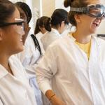 students in lab coats and goggles smiling and laughing together