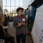 student standing in front of research poster explaining the project to a viewer