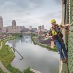 student hanging off a bridge giving a thumbs up while doing construction