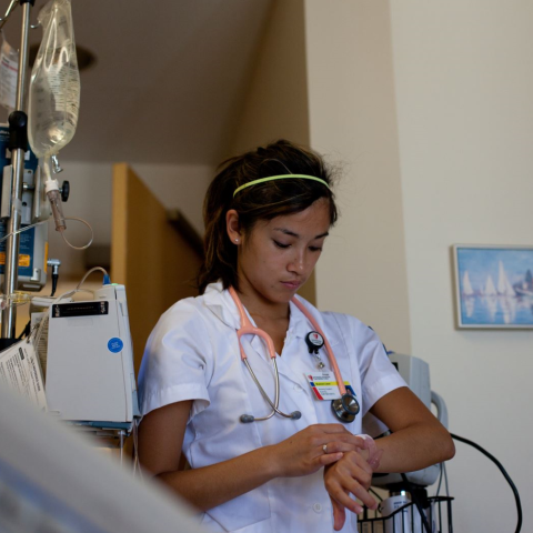 Nursing student in patient's room, looking at watch on wrist