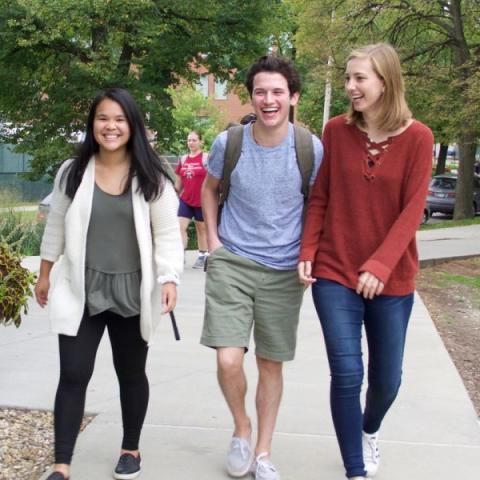 Three students walking outside together, smiling and laughing