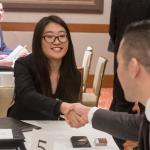 An asian business student at a table shaking hands with business individuals 