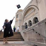 a female student throwing her graduation cap on the steps of a building in her graduation attire