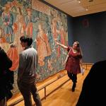 Student walking a group though the art museum and pointing out a tapestry 