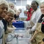 a group of students in hair nets volunteering in a kitchen 