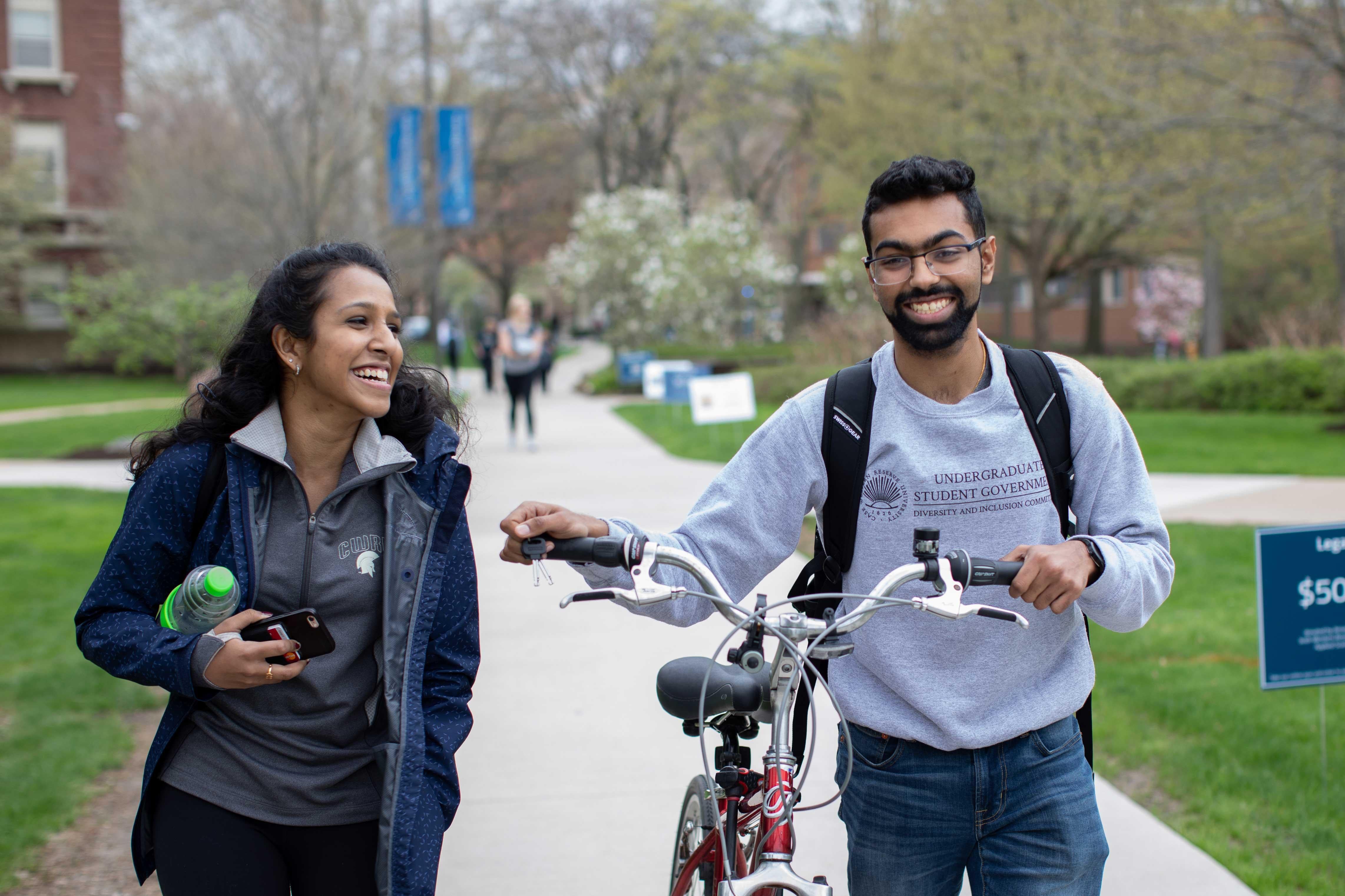 Two students walking and laughing, one with a bike