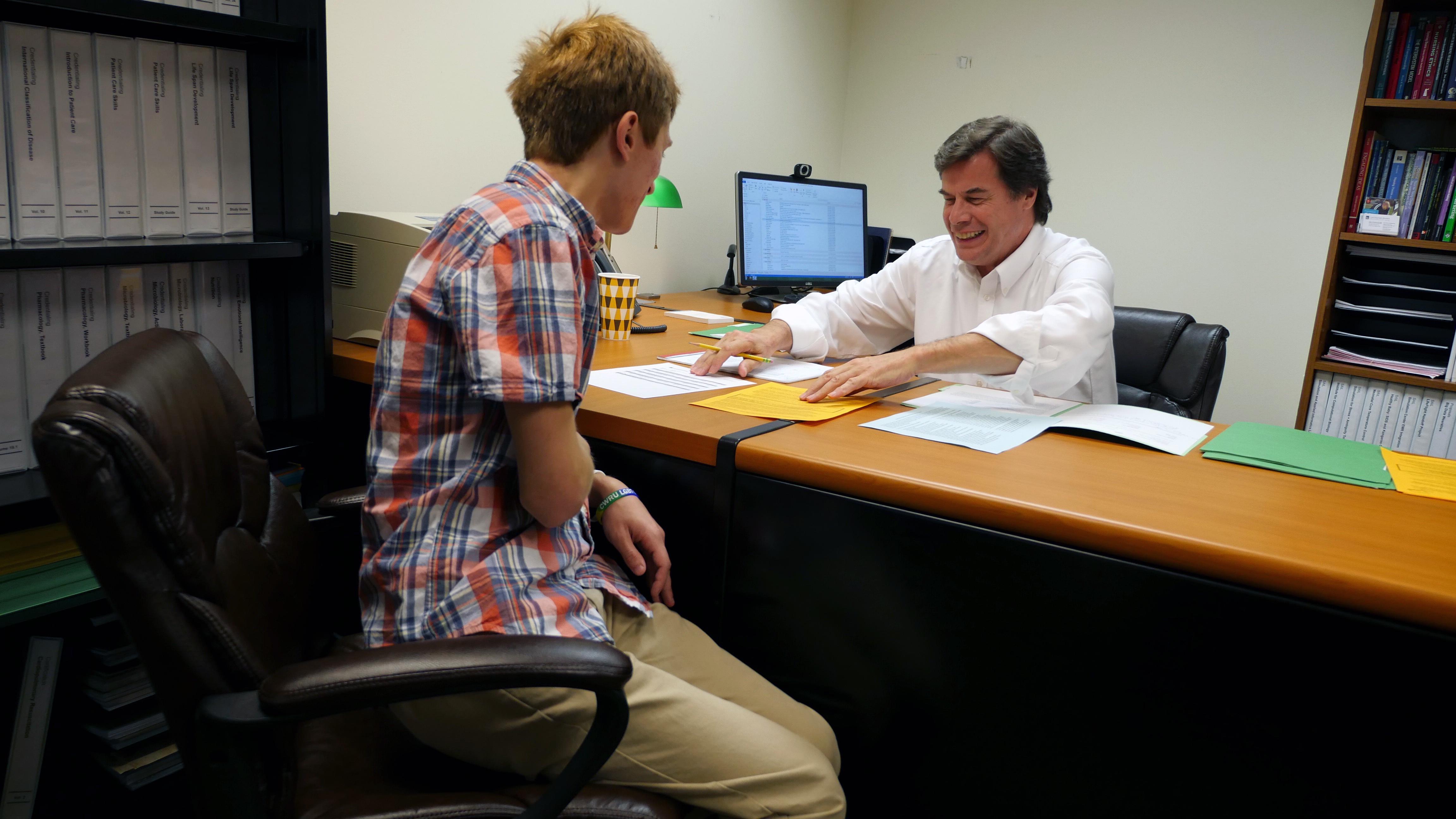 white male faculty member at desk with a white male student
