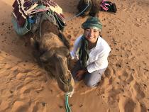Student smiling next to a camel in the desert
