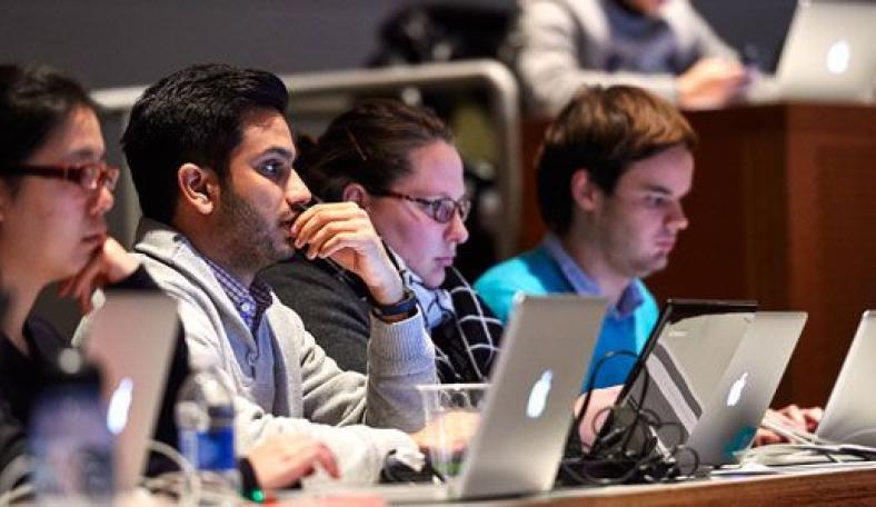Row of students sitting in a lecture hall with laptops