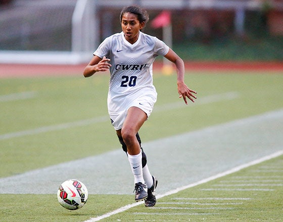 Student running down the field kicking a soccer ball