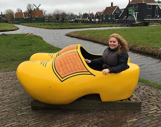 Female student sitting in a wooden shoe while visiting Holland